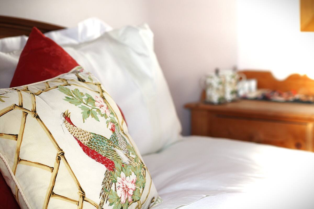 Una cama con sábanas blancas y un cojín decorativo con diseño floral.