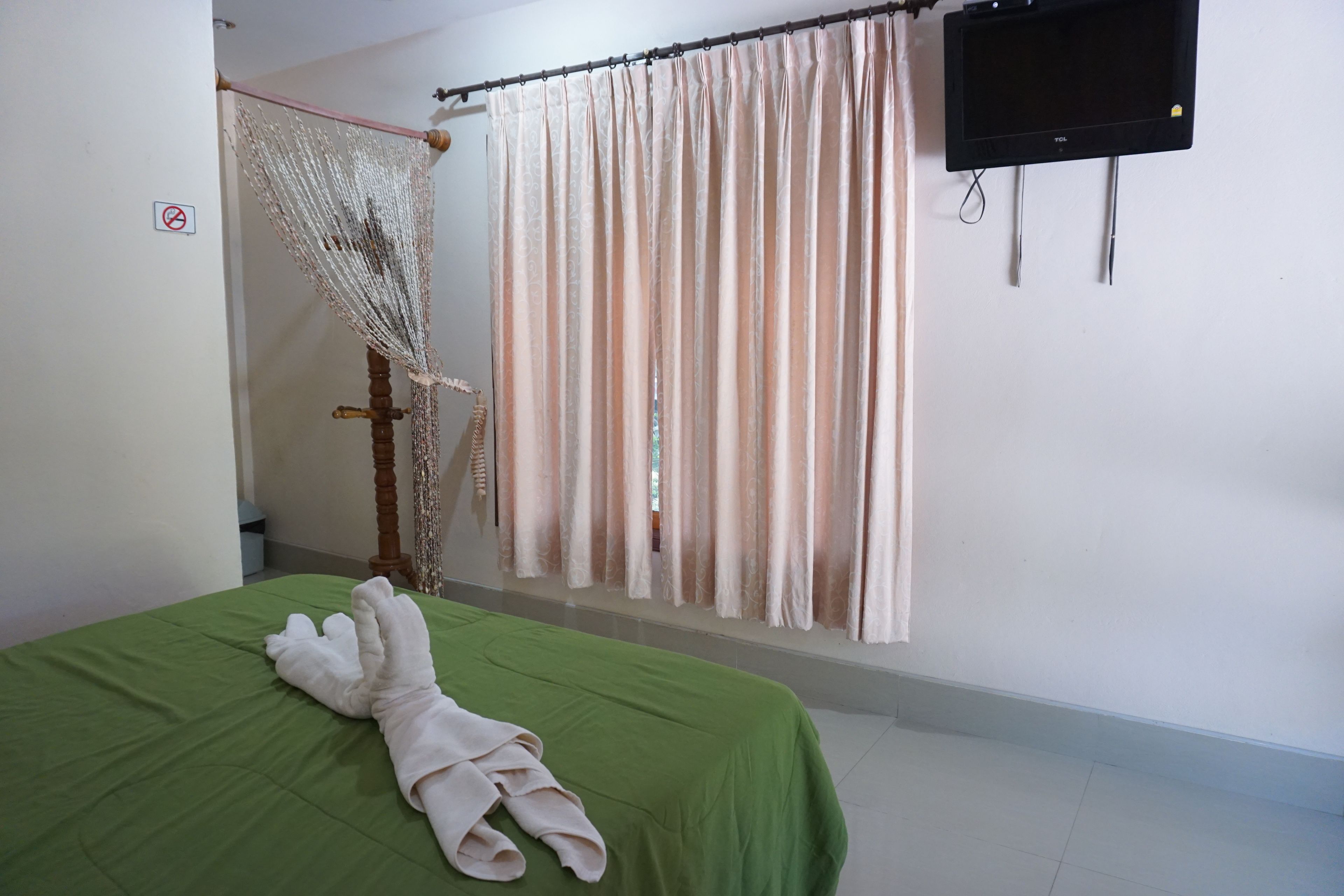 A room with a green bed, a hanging chair, a curtain, and a TV mounted on the wall.
