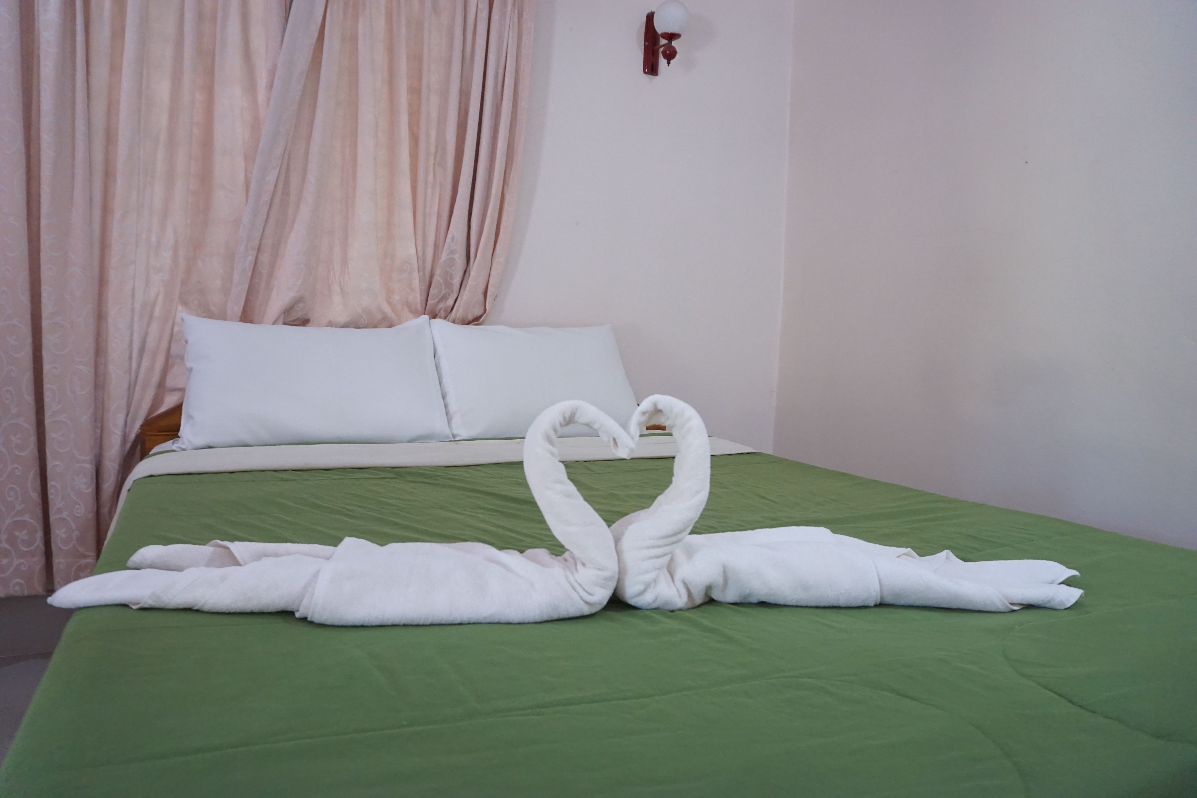 A neatly made bed with green bedding and two swan-shaped towels on the bed.
