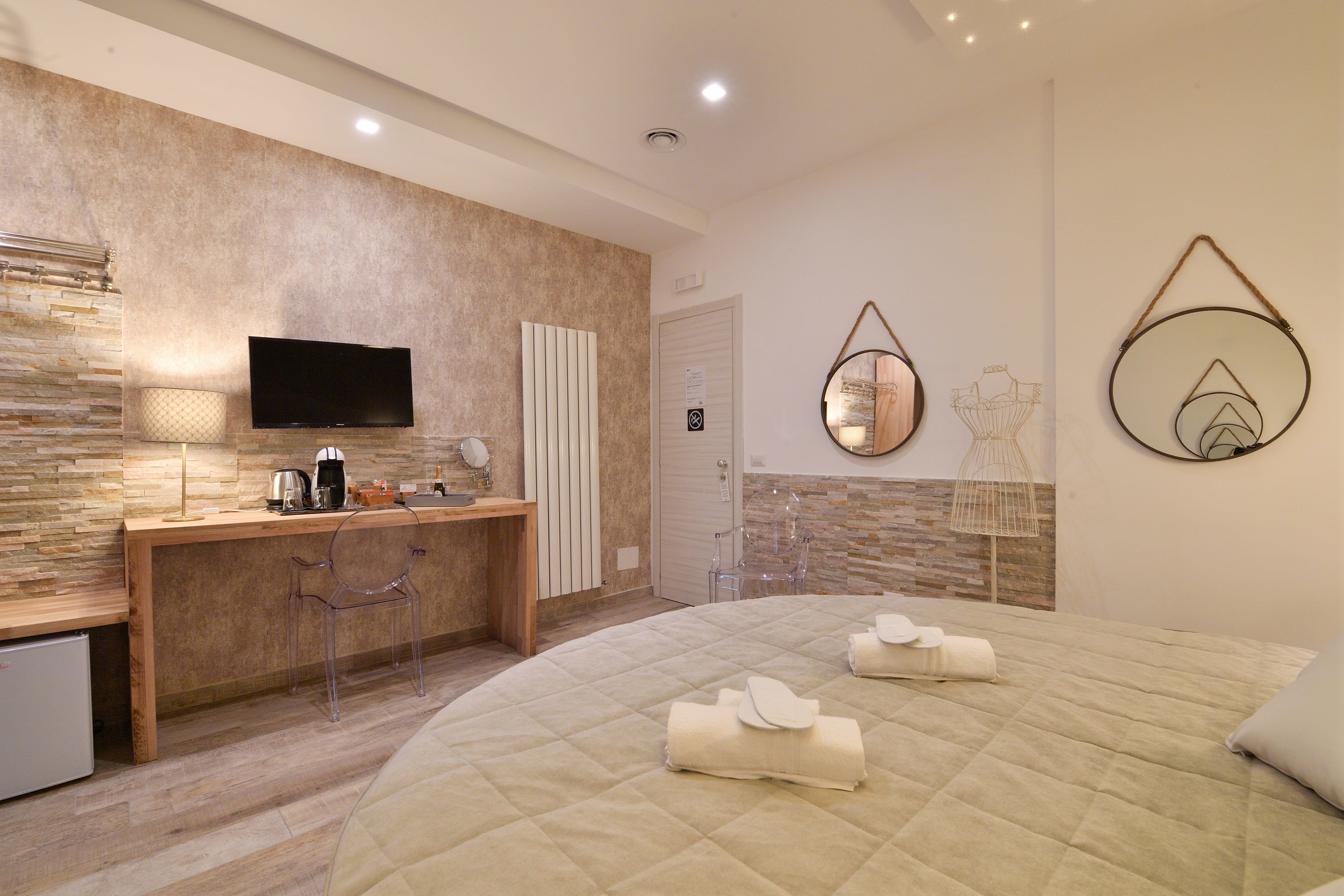 A modern bedroom with a large bed, a wooden desk, a flat-screen TV, and a stone-textured wall.