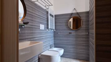 Une salle de bain moderne avec un grand miroir, deux toilettes, un lavabo et un porte-serviettes.