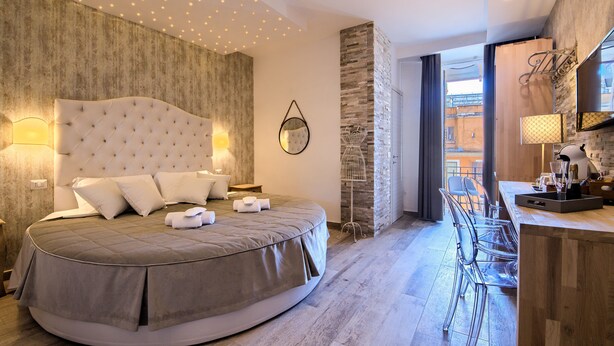 A modern bedroom with a round bed, a wooden accent wall, and a breakfast bar with clear chairs.