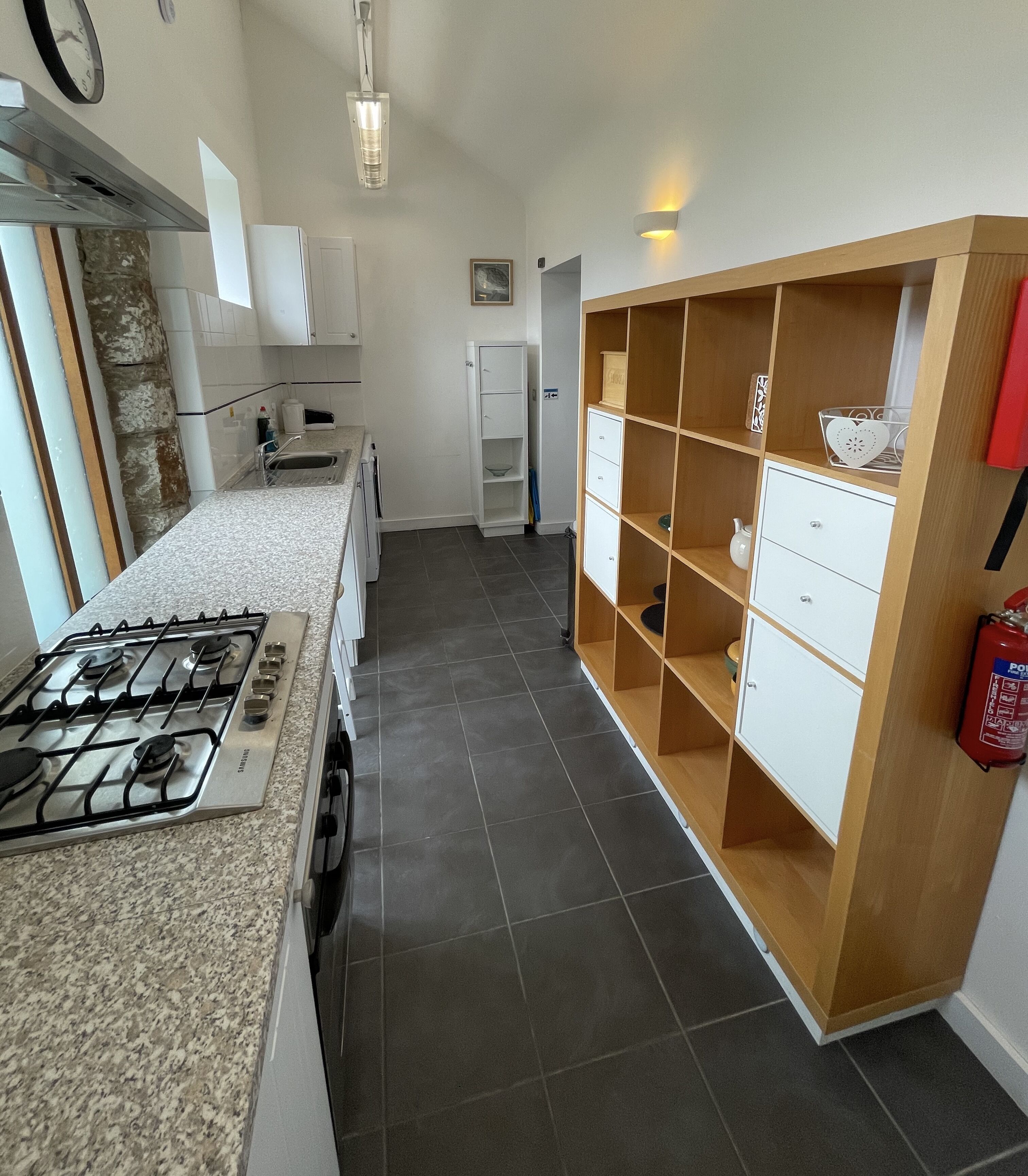 Una cocina moderna con estufa a gas, armarios blancos y una unidad de estanterías de madera.