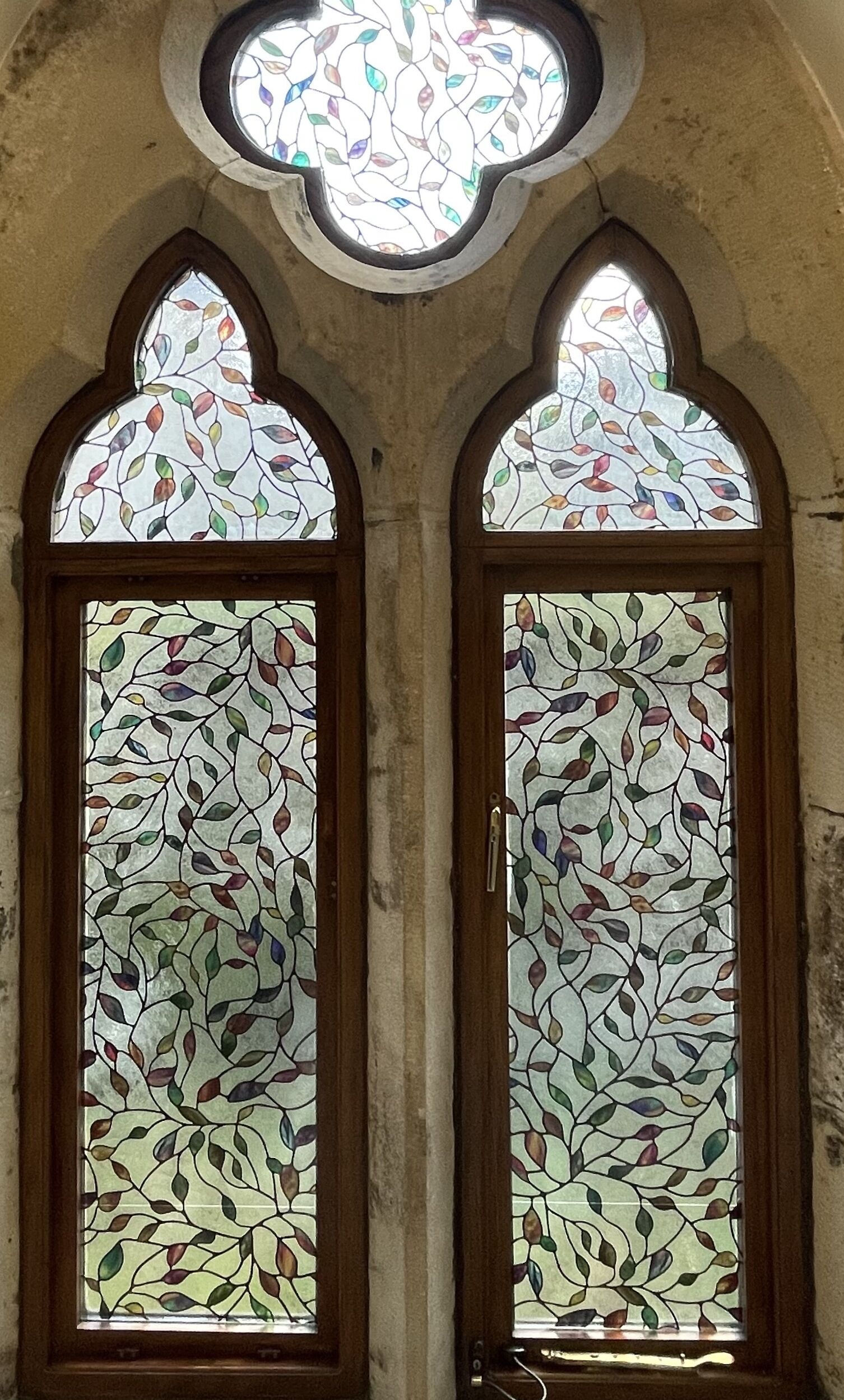 Two stained glass windows with a leaf pattern, set in a stone wall with a circular skylight above.