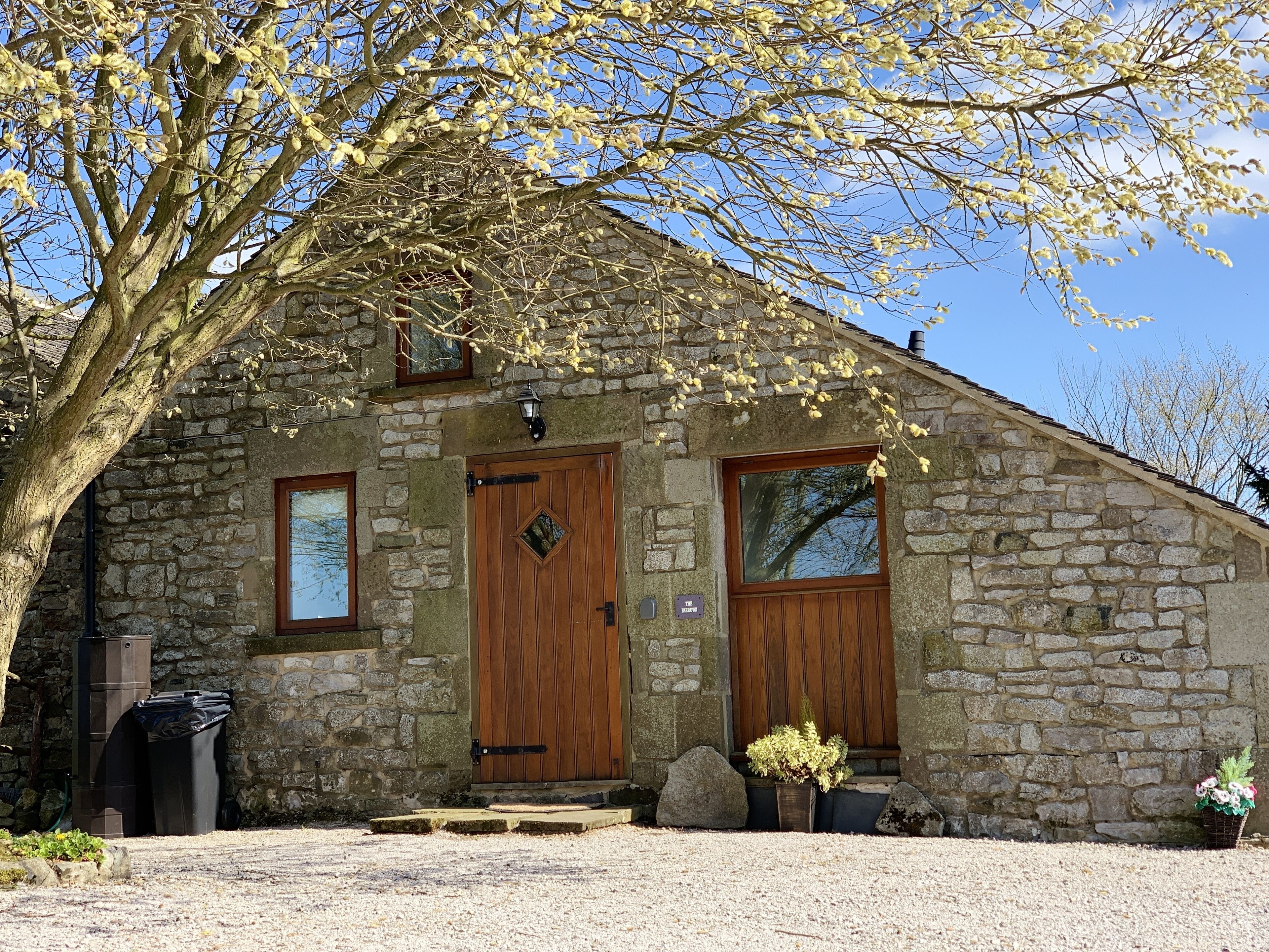A stone building with a wooden door, two windows, and a small porch area with potted plants.