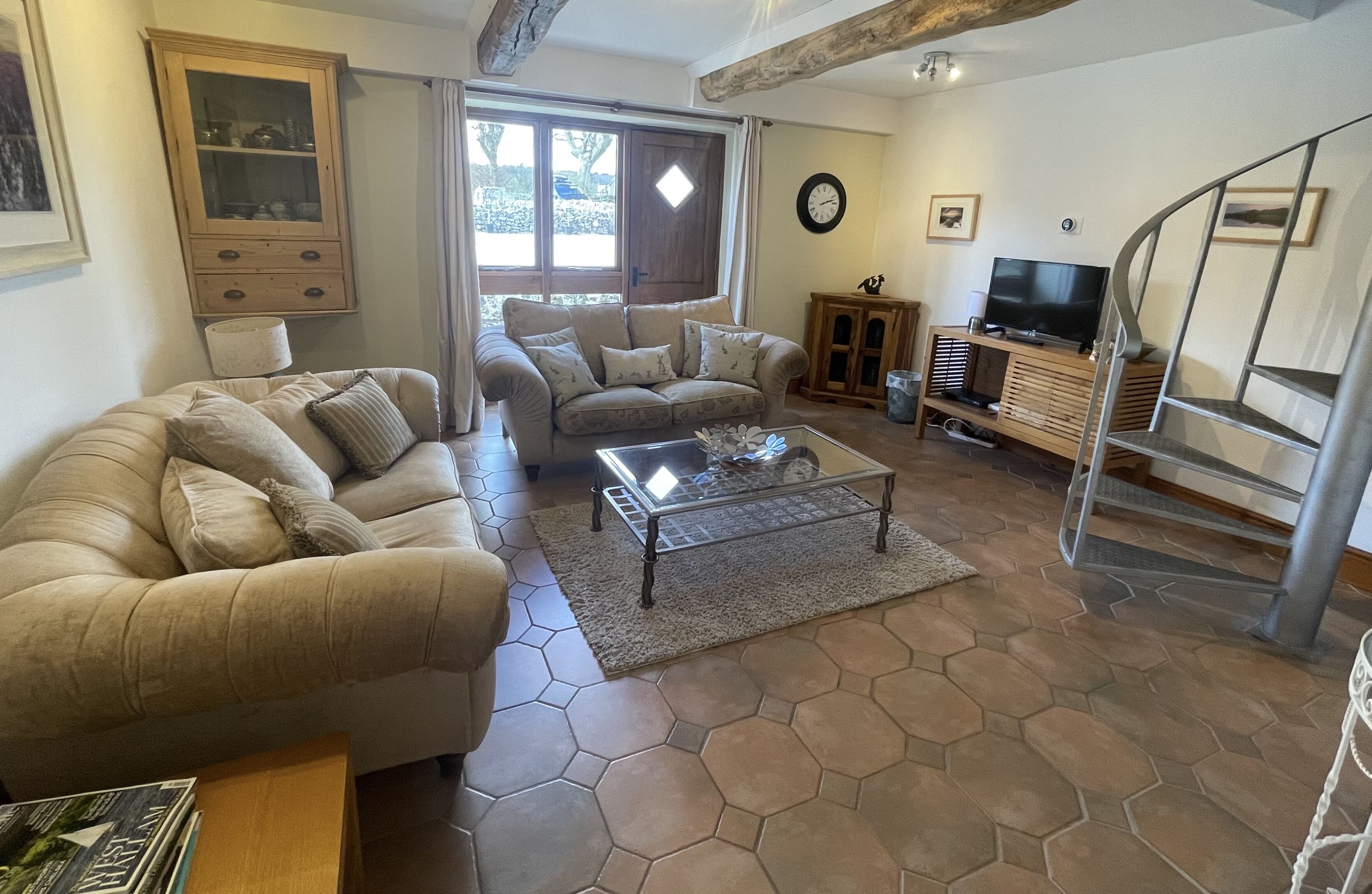 A living room with a sofa, a coffee table, a cabinet with a TV, and a staircase.