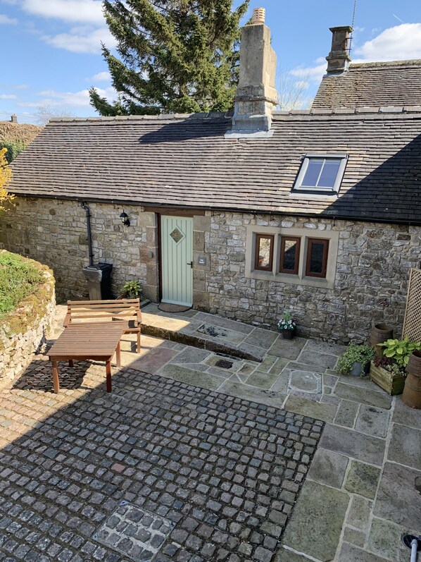 A stone cottage with a tiled patio, a wooden bench, and a door with a window above it.