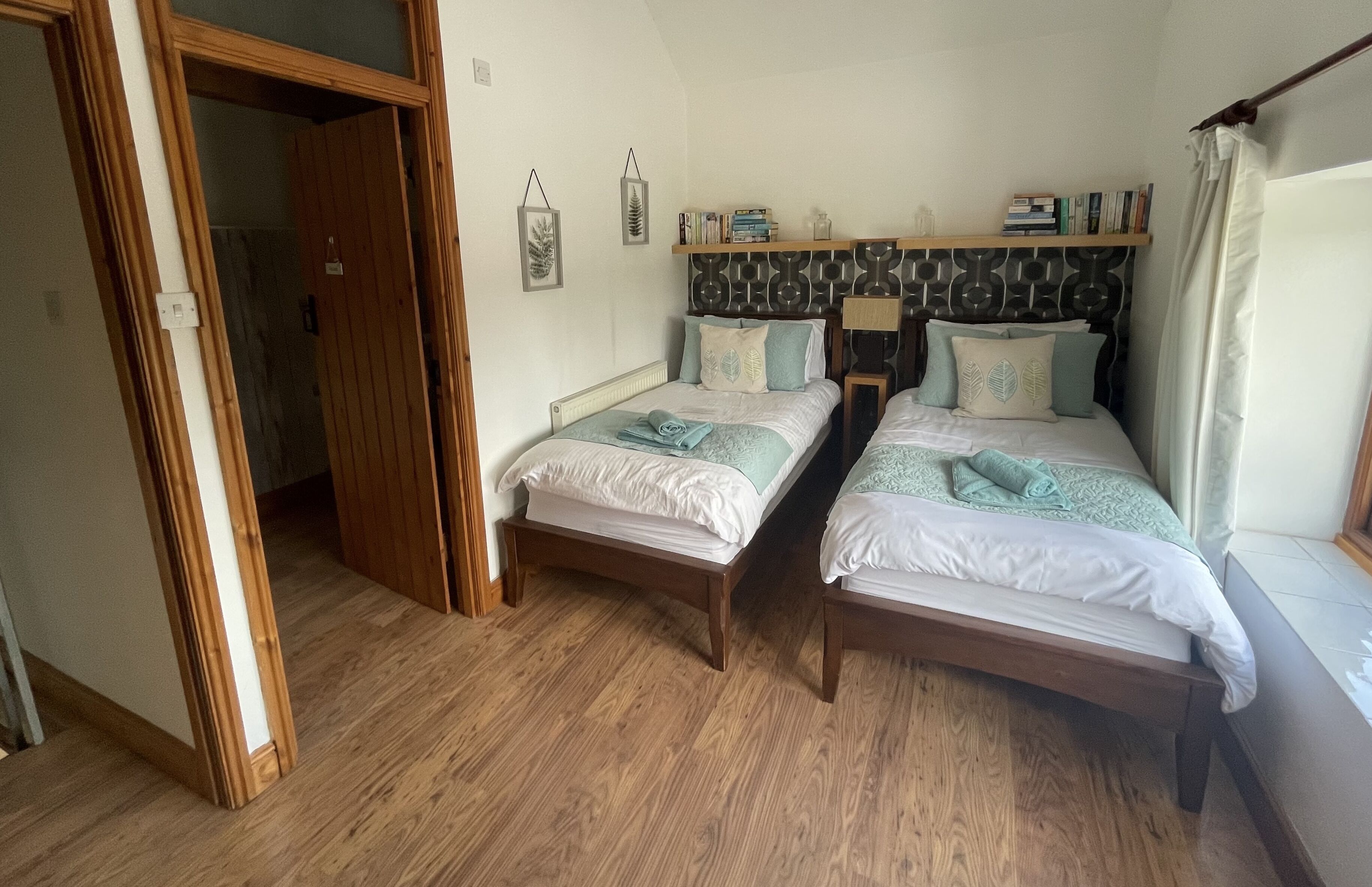 Une chambre avec deux lits en bois, une armoire en bois et une étagère contenant des livres et des objets décoratifs.