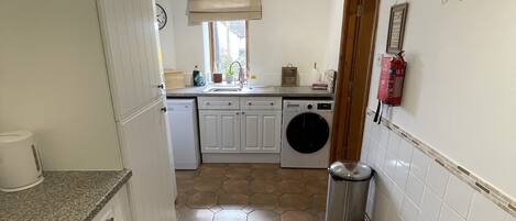 A kitchen with a washing machine, a trash bin, and a fire extinguisher.