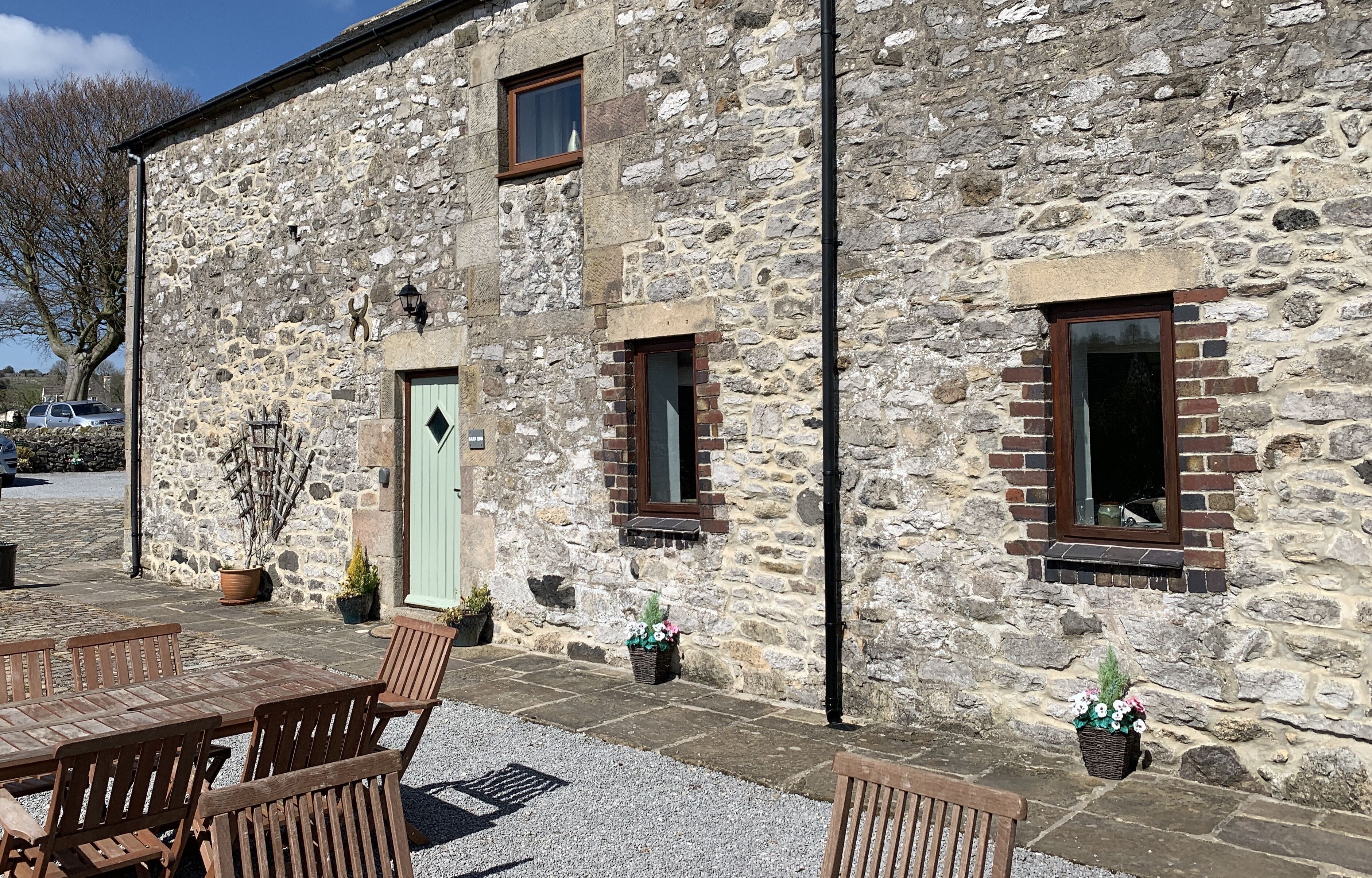 A stone building with a green door, two windows, and outdoor seating.
