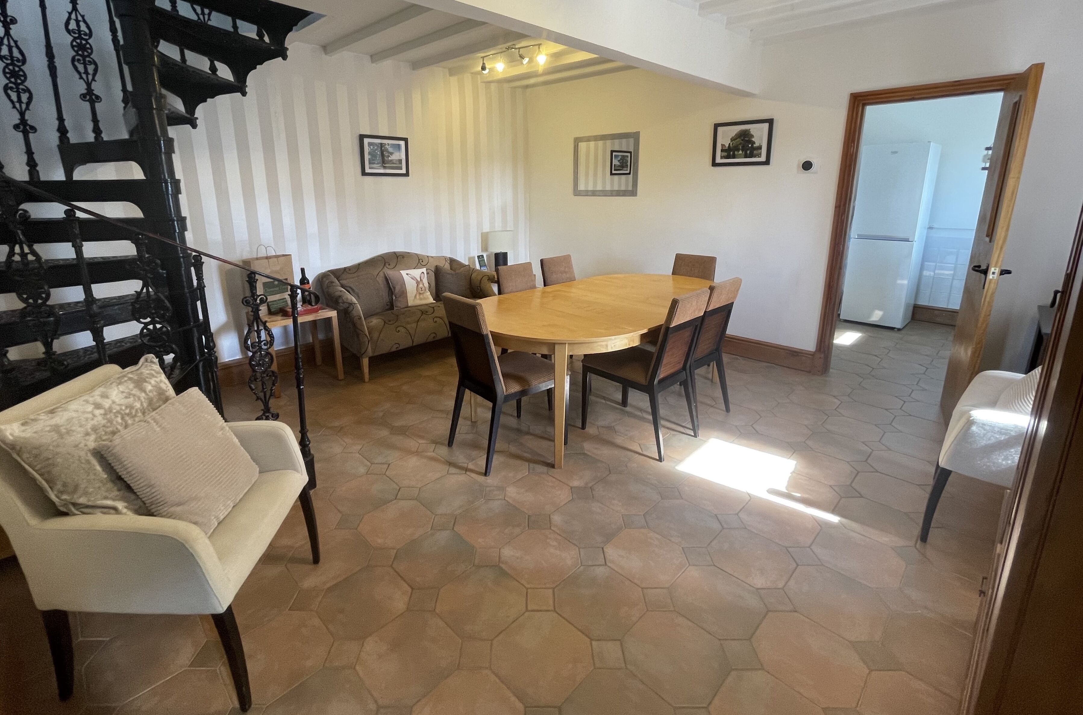 A dining area with a round wooden table and chairs, a sofa, and a staircase.