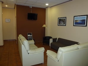A room with two white leather sofas, a television mounted on the wall, and two framed pictures.