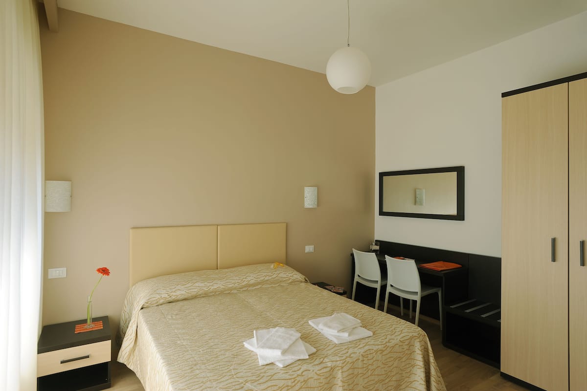 A hotel room with a bed, a desk, a chair, and a wardrobe.