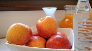 Un tazón de manzanas y una botella de jugo de naranja sobre una mesa.