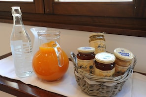Uma mesa com uma garrafa de água, um jarro de suco de laranja e uma cesta com potes de mel.