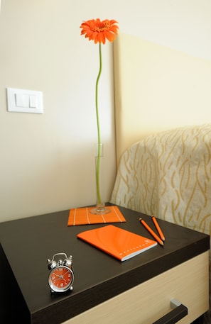 Uma mesa com um vaso contendo uma única flor, um relógio e um caderno laranja.