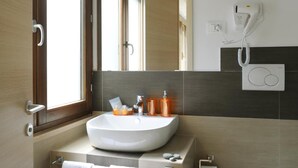 Un baño moderno con lavamanos blanco, espejo, secador de pelo y inodoro.