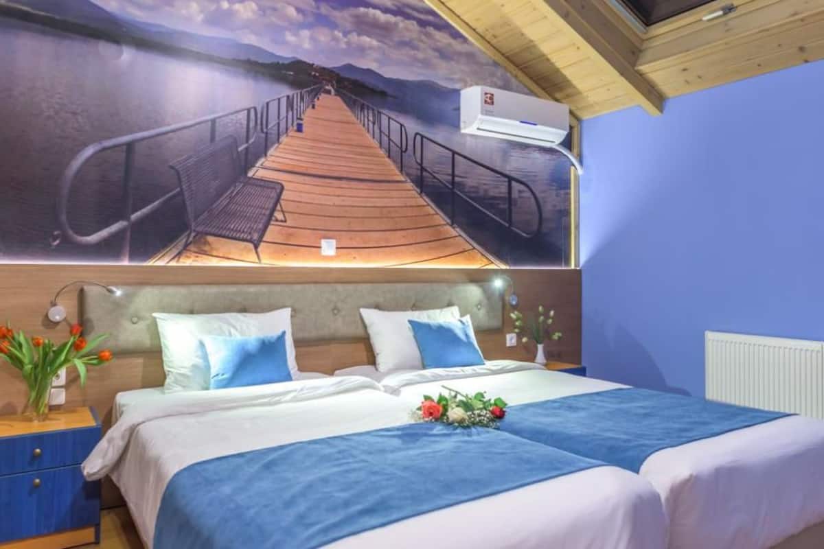 A bedroom with a bed, a nightstand, a wall-mounted air conditioner, and a mural of a pier.