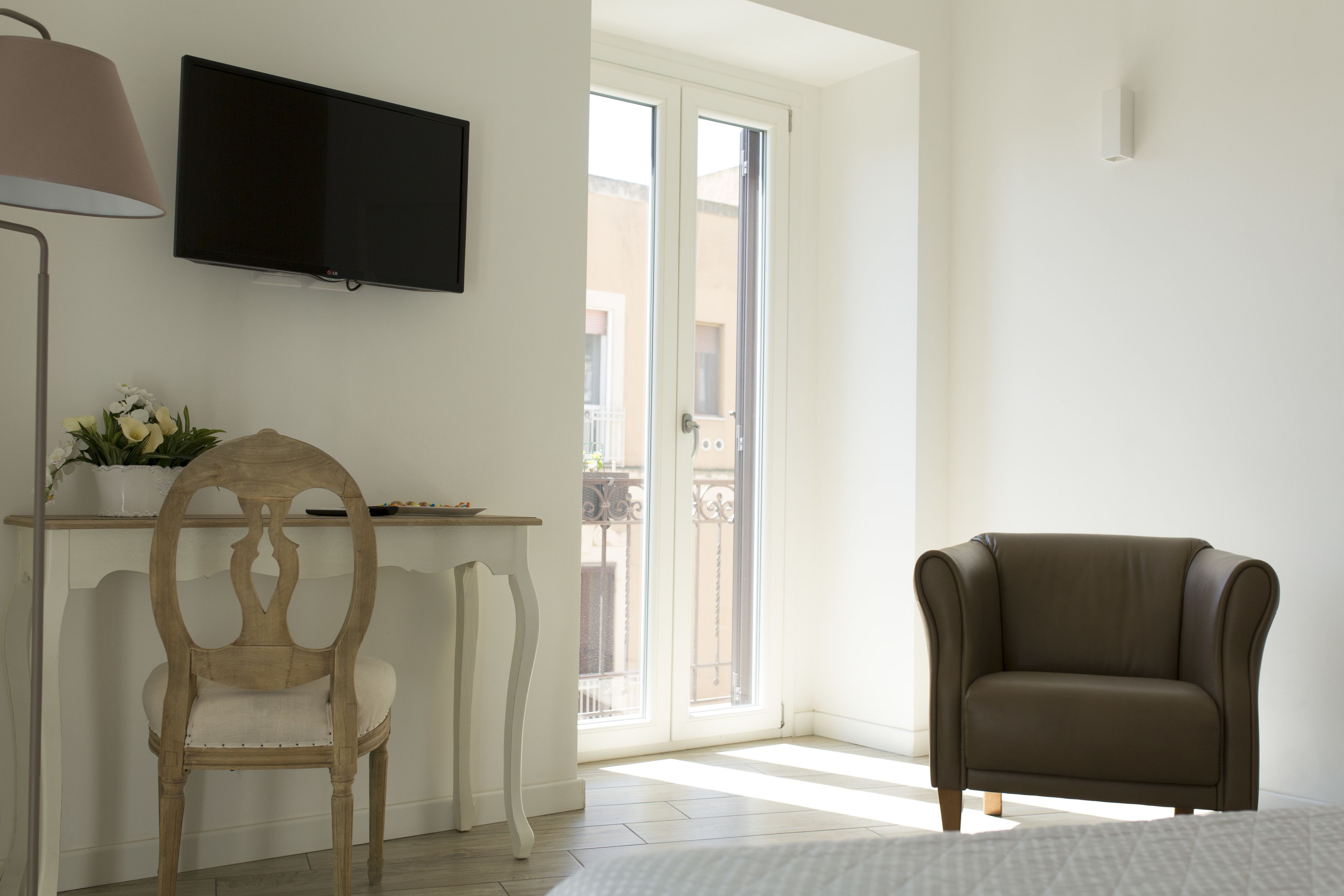Una habitación con una televisión montada en la pared, una silla de madera, un sofá y una ventana con vistas a edificios.
