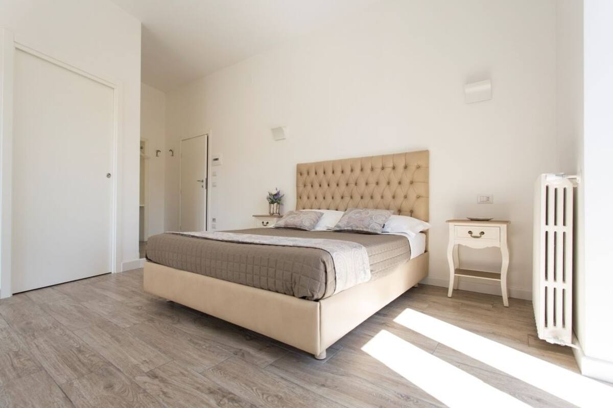 A bedroom with a bed, bedside tables, a radiator, and a door.