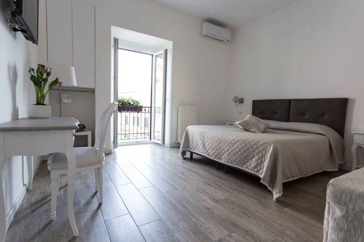 A bedroom with a bed, a desk, a chair, a radiator, and a view of the outside.