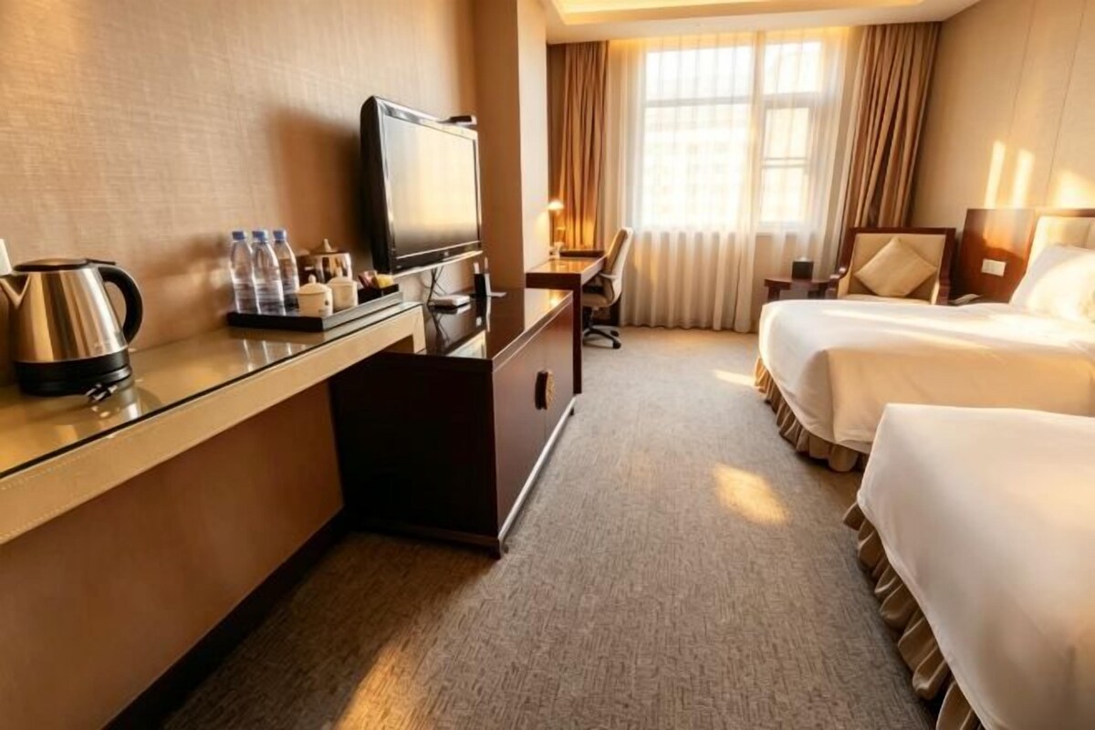 Una habitación de hotel con escritorio, televisor, cama y ventana con cortinas.