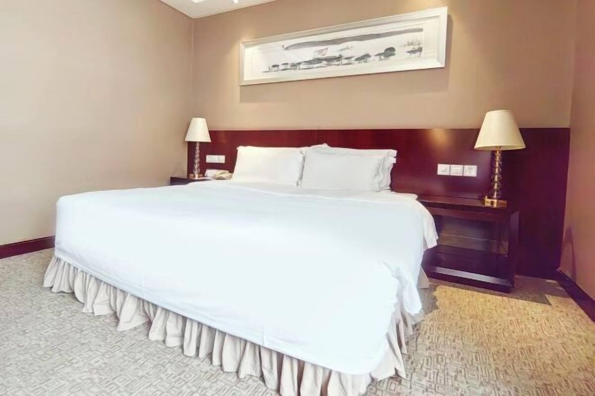 Une chambre d’hôtel avec un grand lit, deux tables de chevet avec des lampes, une tête de lit et un tableau encadré au mur.