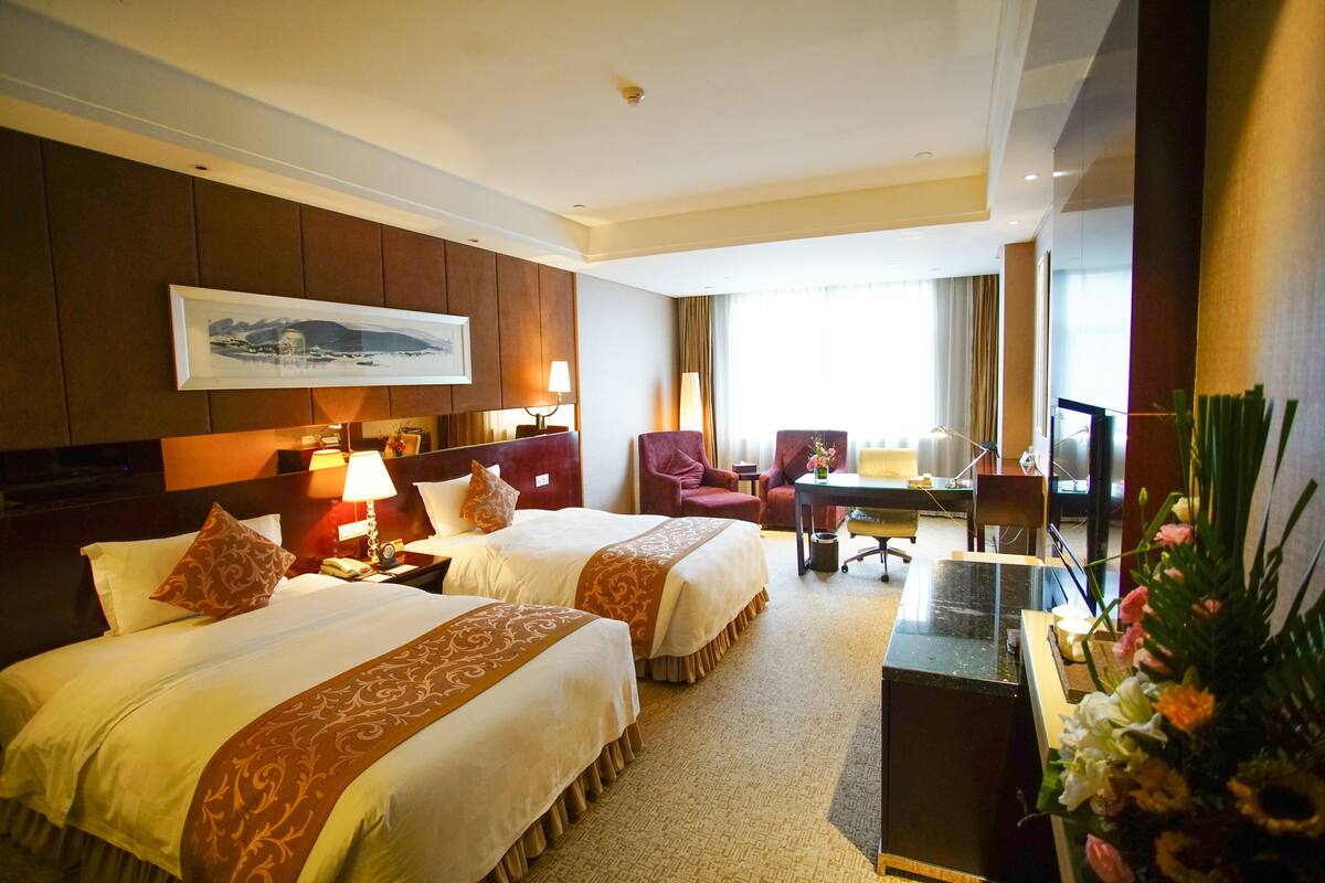 Une chambre d’hôtel avec deux lits, un bureau, une chaise, une télévision et une grande fenêtre.
