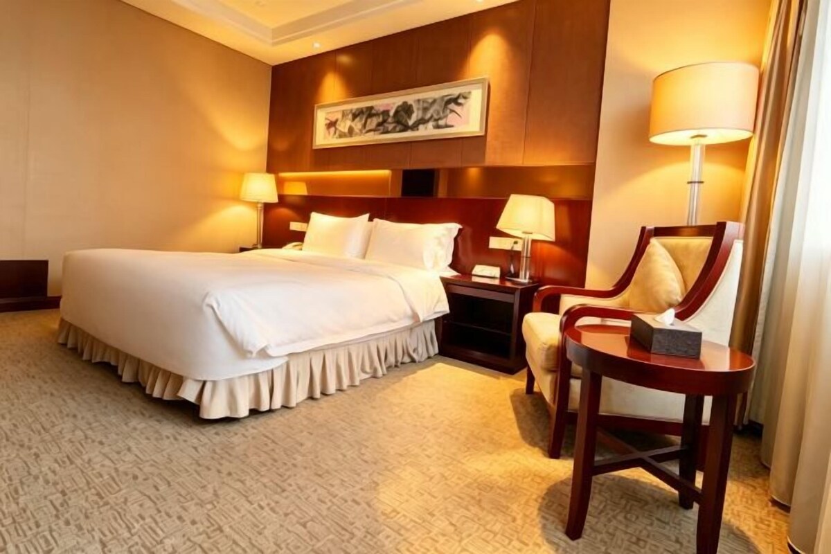 A hotel room with a large bed, bedside tables, a chair, and a lamp.