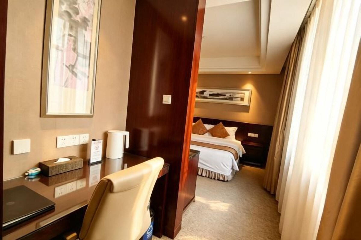 Habitación de hotel con escritorio, silla, cama y vista al pasillo.