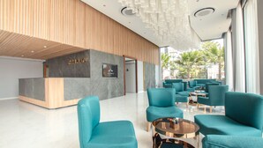 A modern hotel lobby with teal seating, a reception desk, and a large window offering a view of the outdoors. - Hotel MAYU Chiang Mai (Chiang Mai)