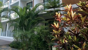 A multi-story hotel with balconies, large windows, and a well-maintained garden with various plants.