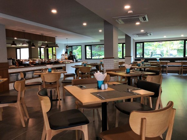 Interior moderno de un restaurante con mesas y sillas de madera, una zona de bar y amplios ventanales con vistas al exterior.