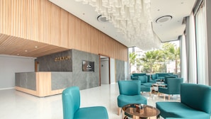 A modern lobby with teal chairs, a reception desk, and a view of palm trees outside.