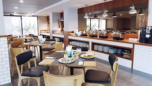 A modern restaurant with wooden tables and chairs, a buffet counter with various food items, and a coffee machine.