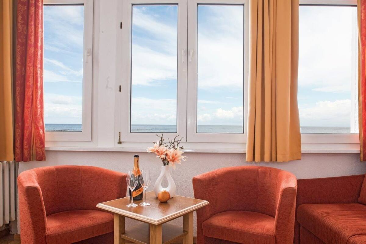 Una habitación con dos sofás rojos, una mesa de madera con una botella y flores, y vistas al mar a través de amplias ventanas.