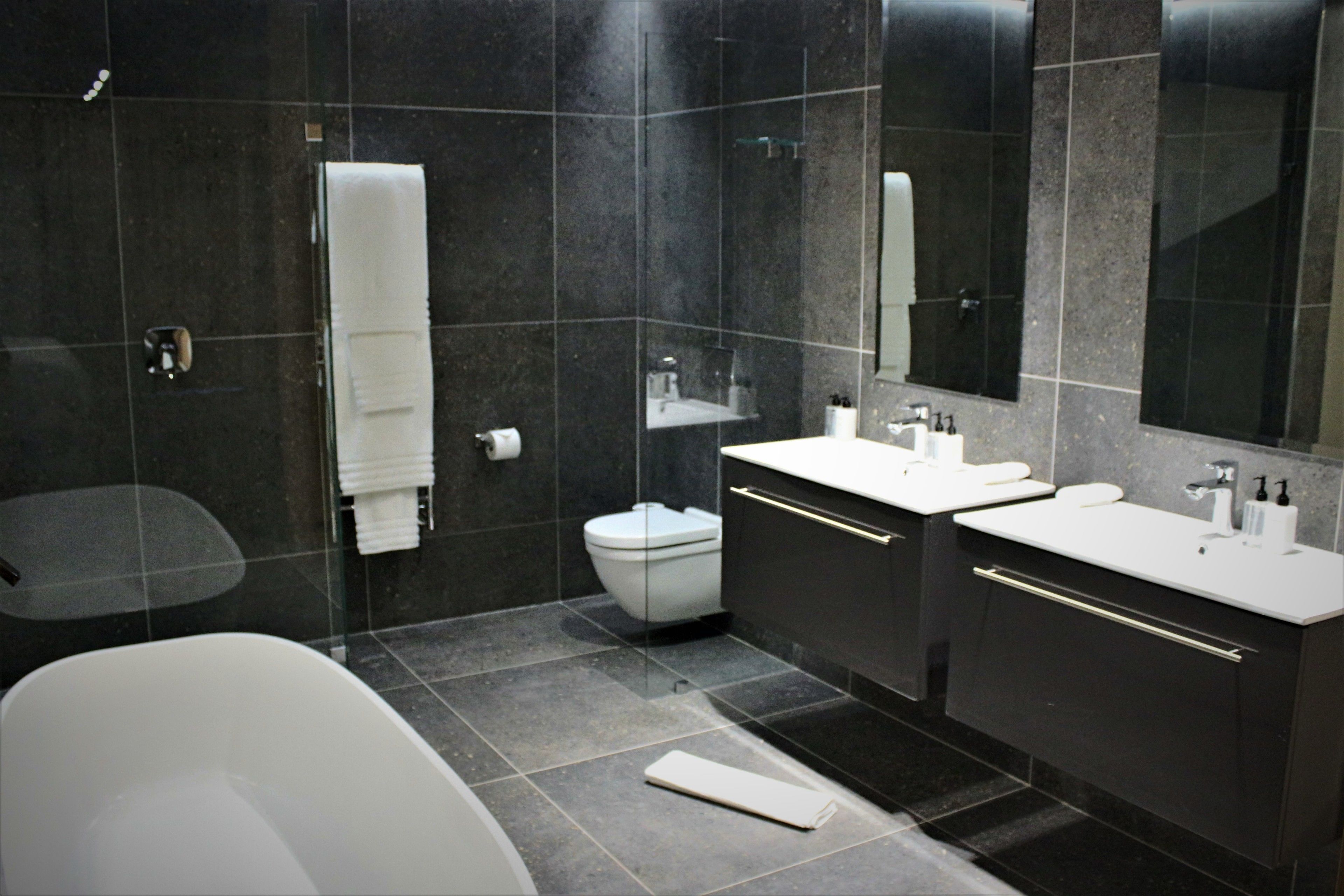Une salle de bain moderne avec une baignoire, deux lavabos, des toilettes et un grand miroir.
