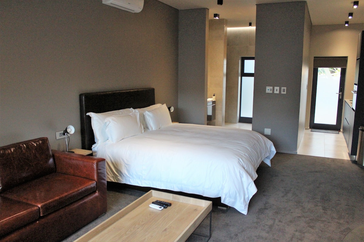A modern hotel room with a large bed, a leather sofa, and a wooden side table.