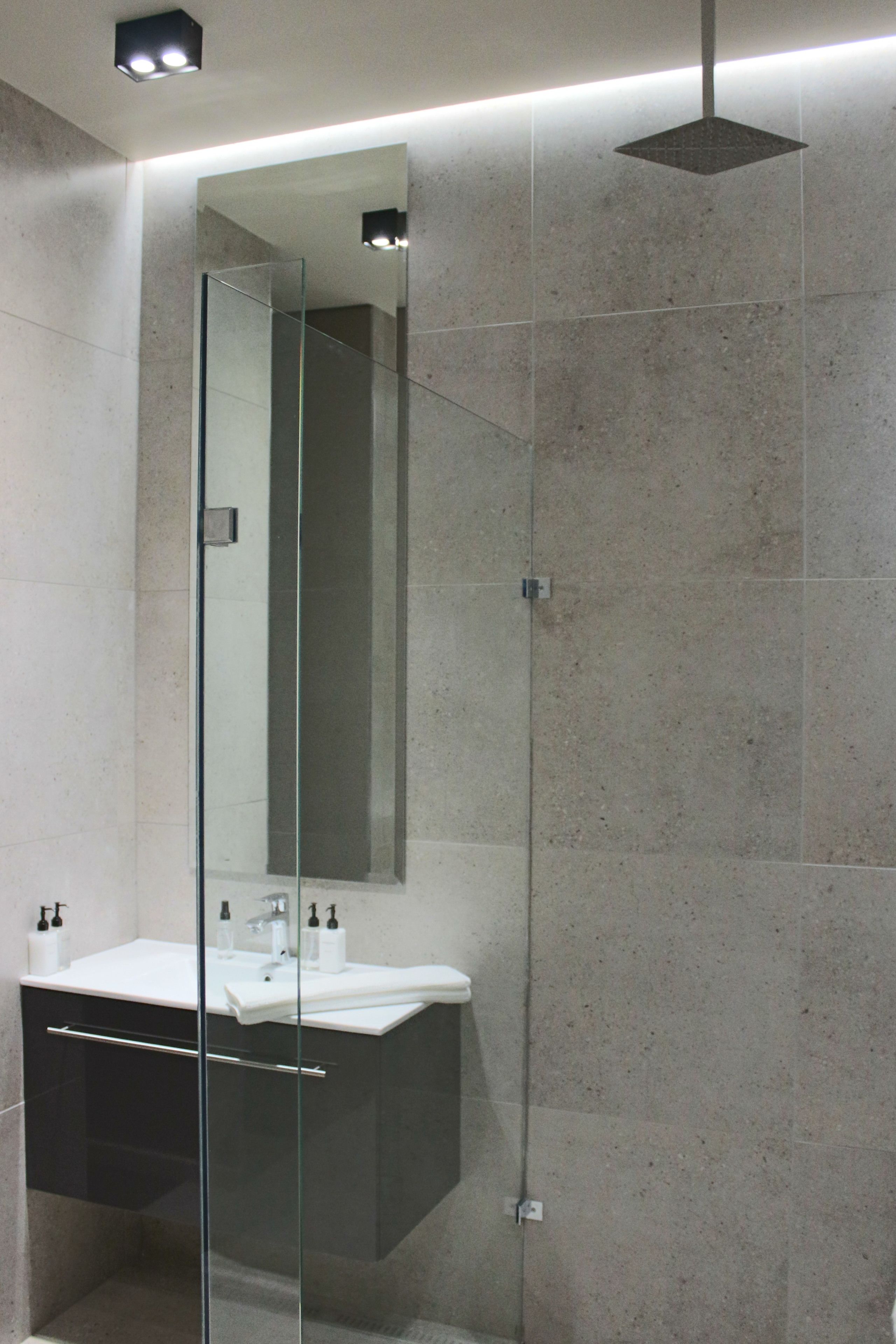 A modern bathroom with a glass-enclosed shower, a large mirror, and a white sink with toiletries.