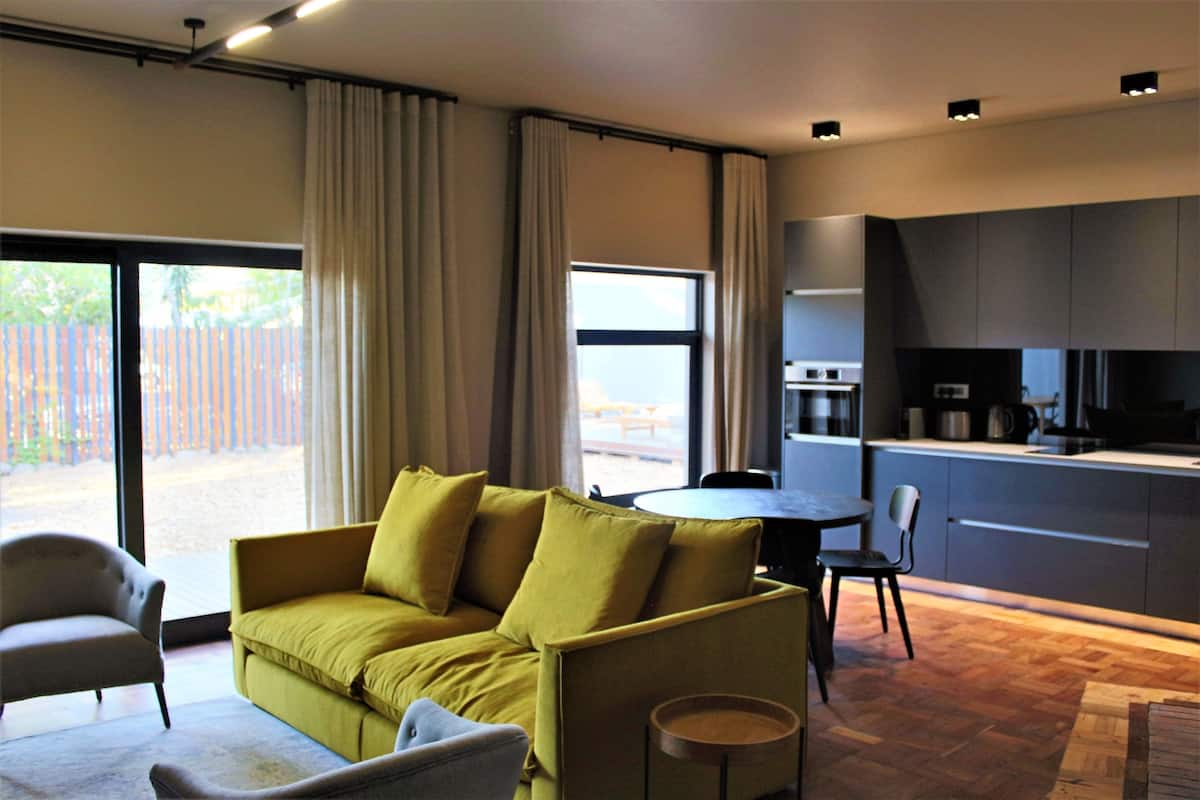 A modern living room with a sofa, chairs, a dining table, and a kitchen area with cabinets and appliances.
