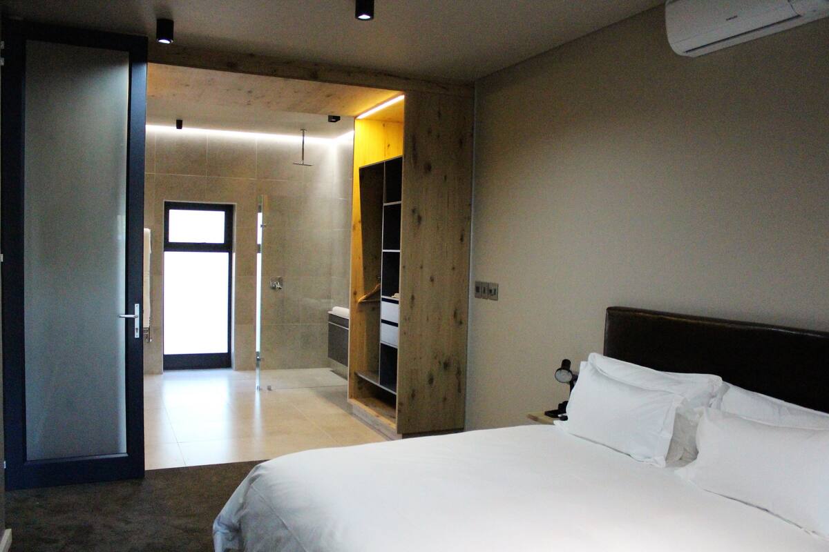 A hotel room with a bed, a wooden wardrobe, and a bathroom visible through an open door.
