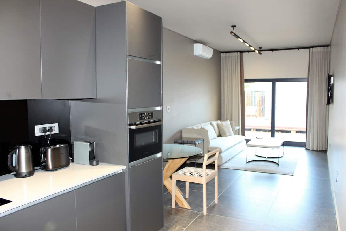 A modern kitchen with a built-in oven and a dining area with a glass table and a sofa.