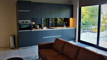 Een moderne keuken met donkere kastjes, een ingebouwde oven en een groot raam met uitzicht op het groen.