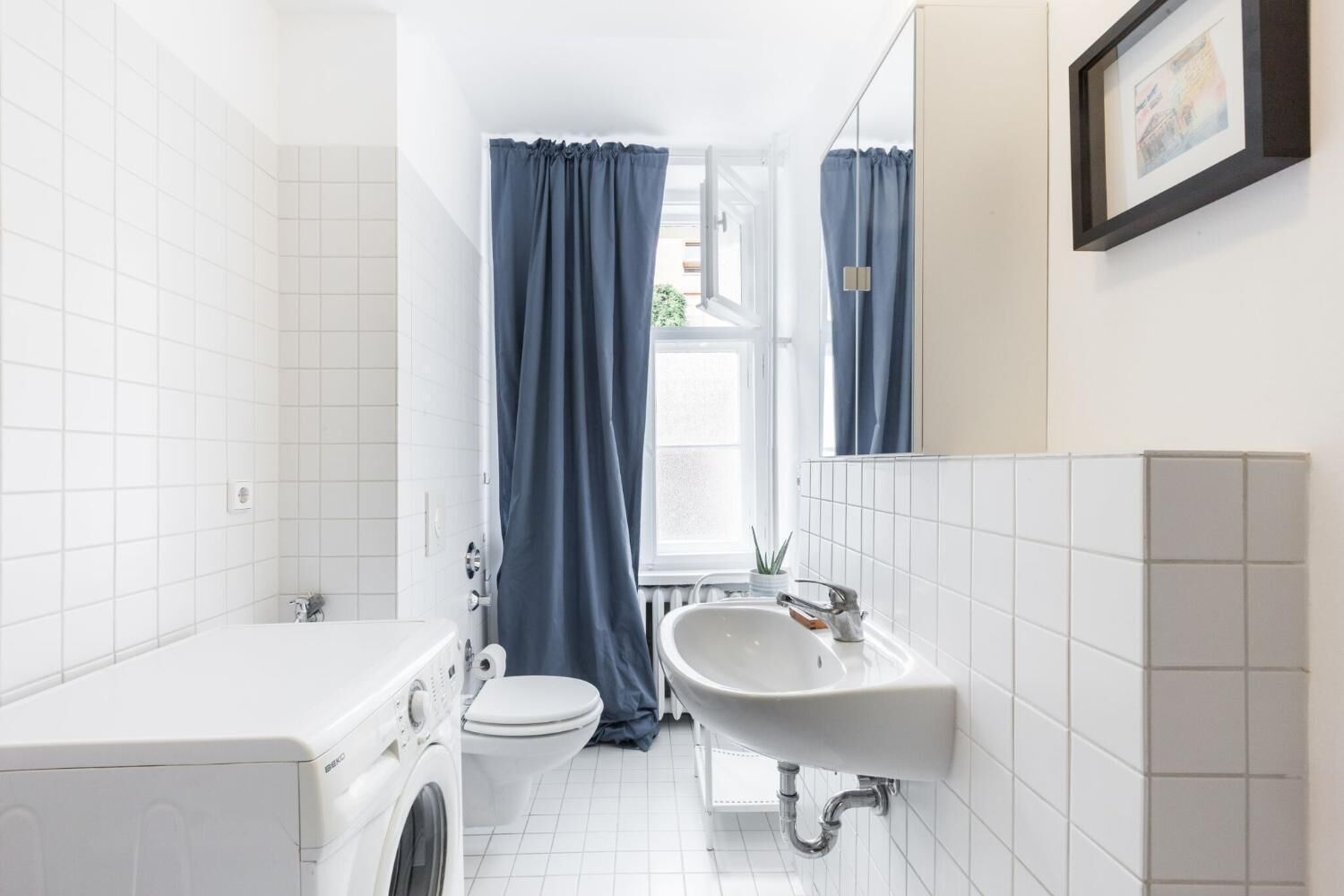 A modern bathroom with a washing machine, toilet, sink, and a window with curtains.