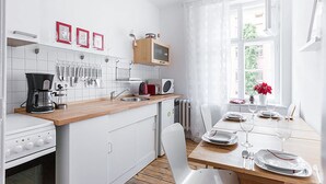 Eine moderne Küche mit weißen Schränken, einer Holzarbeitsplatte, einer Kaffeemaschine, einem Toaster und einem Essbereich mit Tisch für zwei Personen.