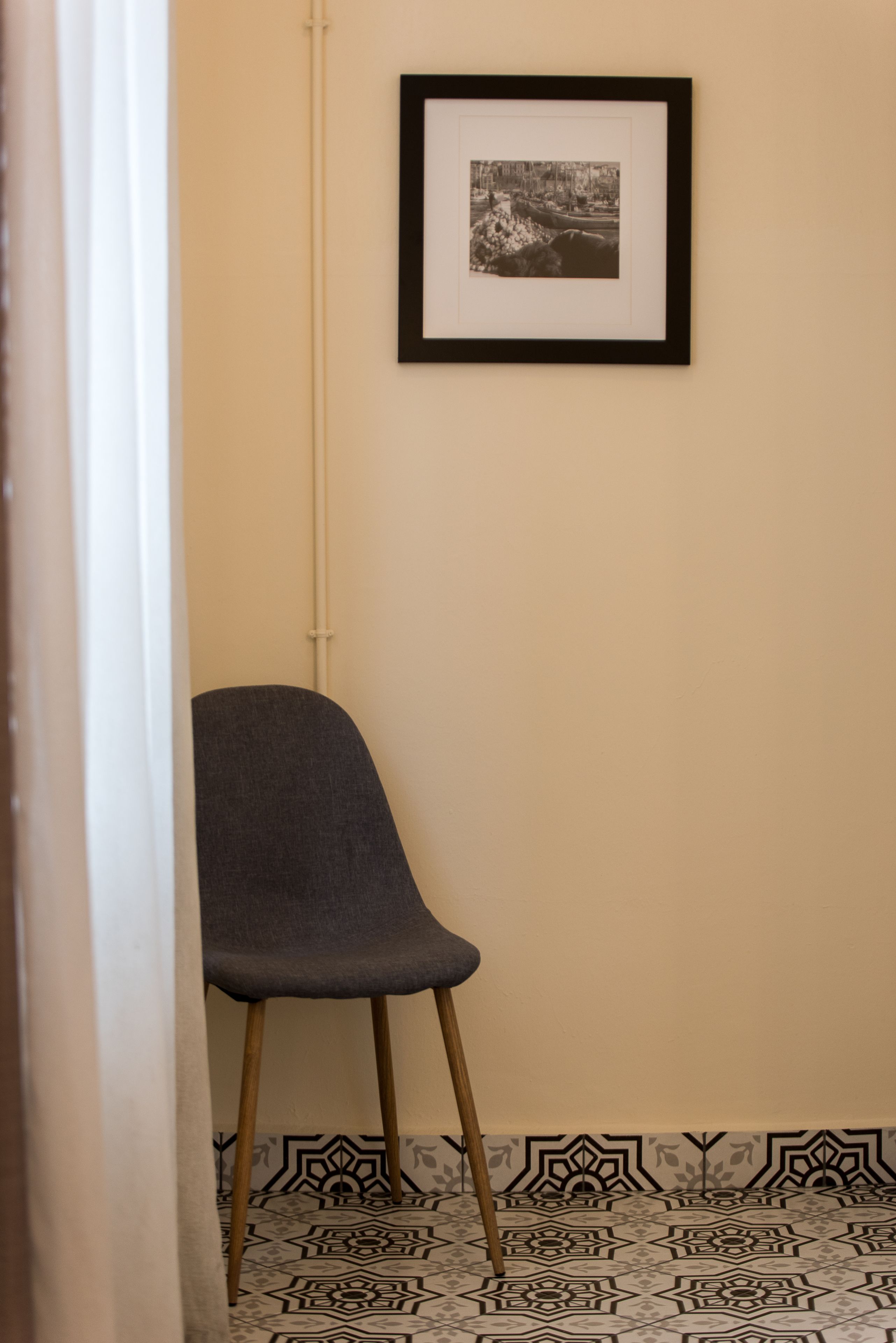 A chair in a corner with a patterned floor and a framed picture on the wall.