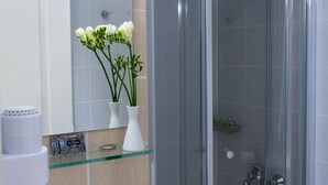 A bathroom with a glass shower enclosure, a white sink, a mirror, and a vase with flowers.