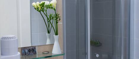 Un baño con cabina de ducha de vidrio, un lavabo blanco, un espejo y un florero con flores.