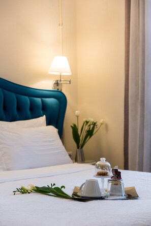A neatly made bed with a blue headboard, a bedside table with a lamp, and a small vase with flowers.