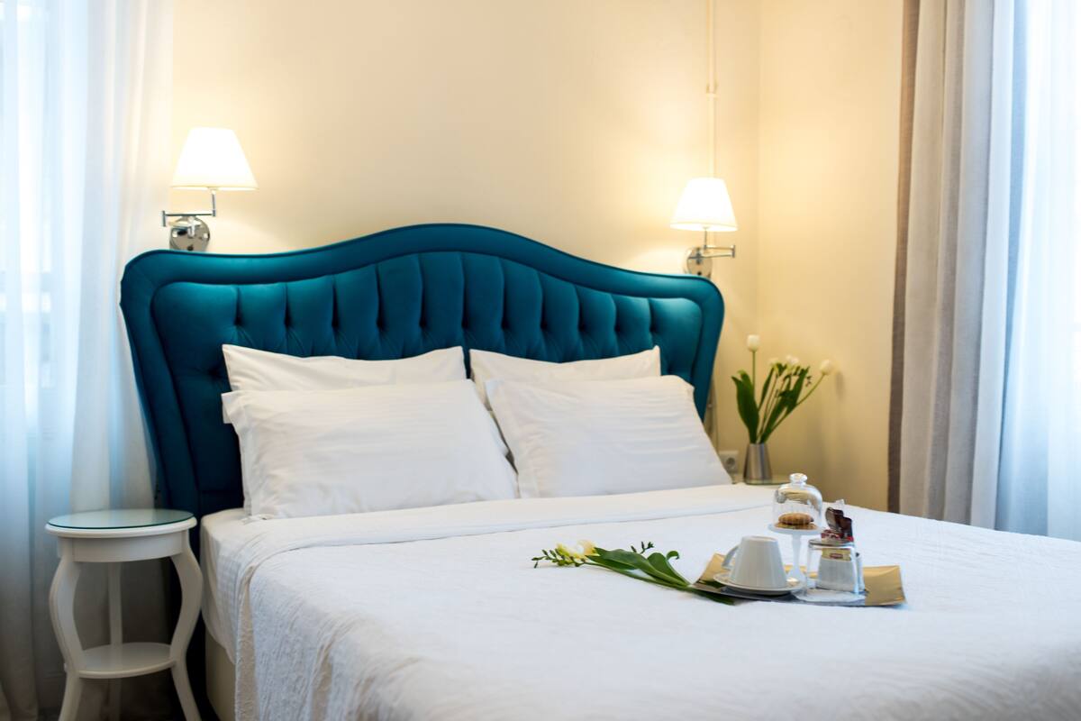 Una cama bien tendida con cabecera color turquesa, ropa de cama blanca y una mesita de noche con una lámpara.